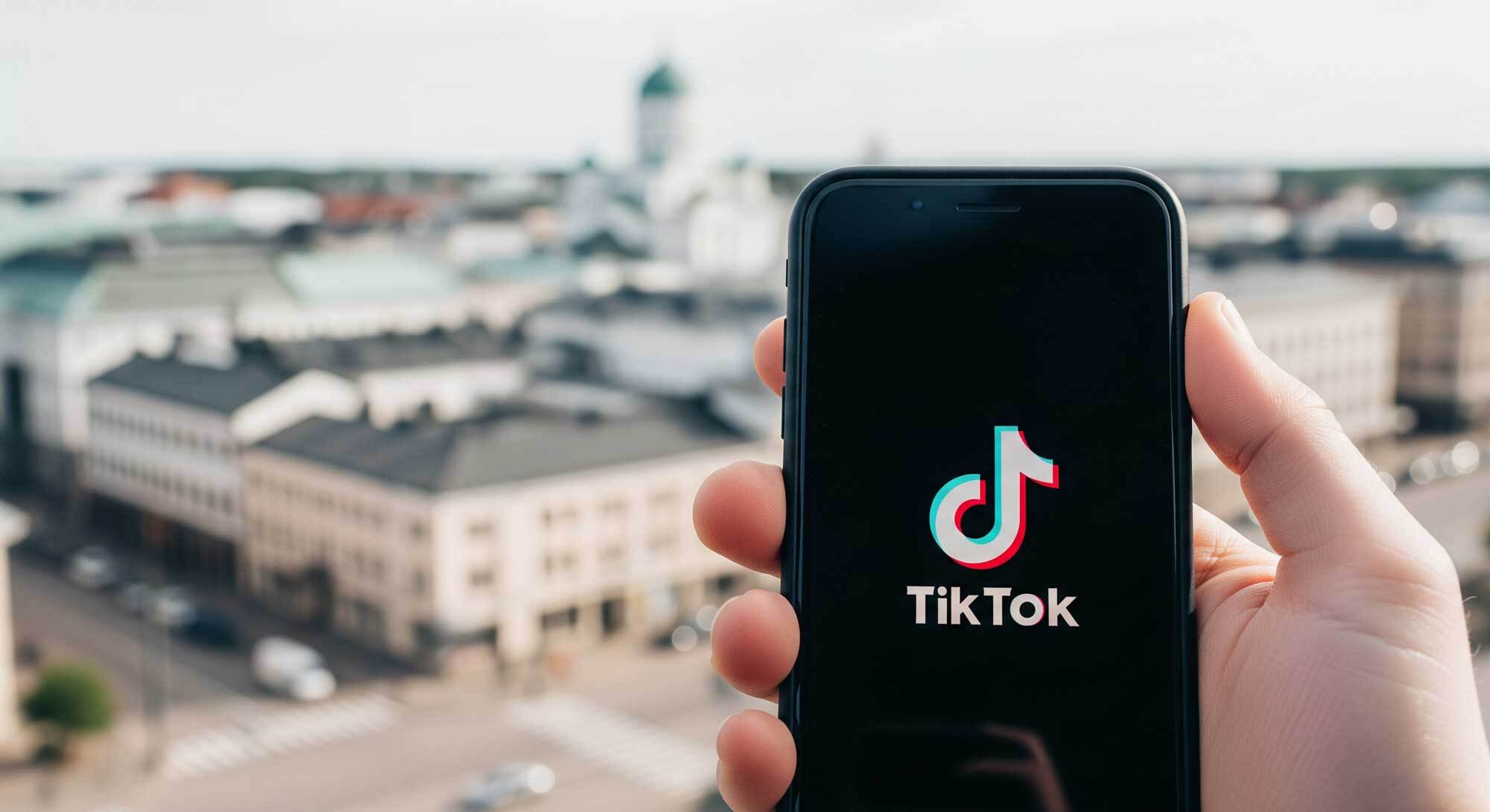 TikTok-sovellu puhelimen näytöllä, taustalla himmeä kaupunkimaisema